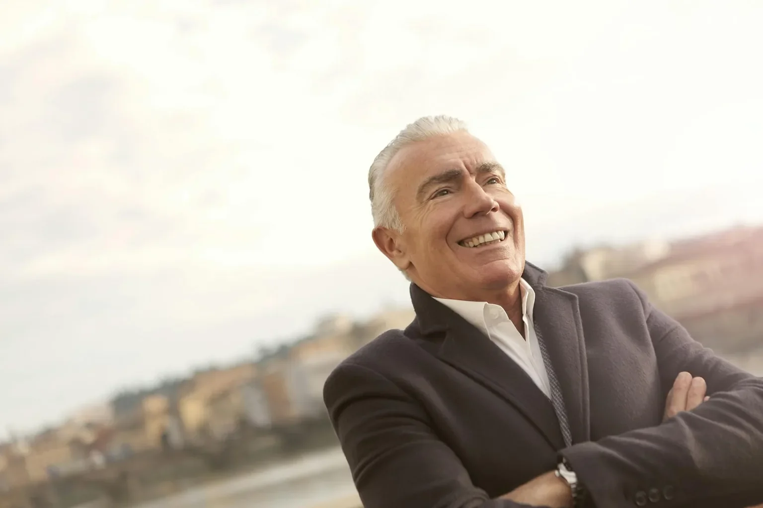 A senior man in business attire smiles confidently during a sunny outdoor setting.