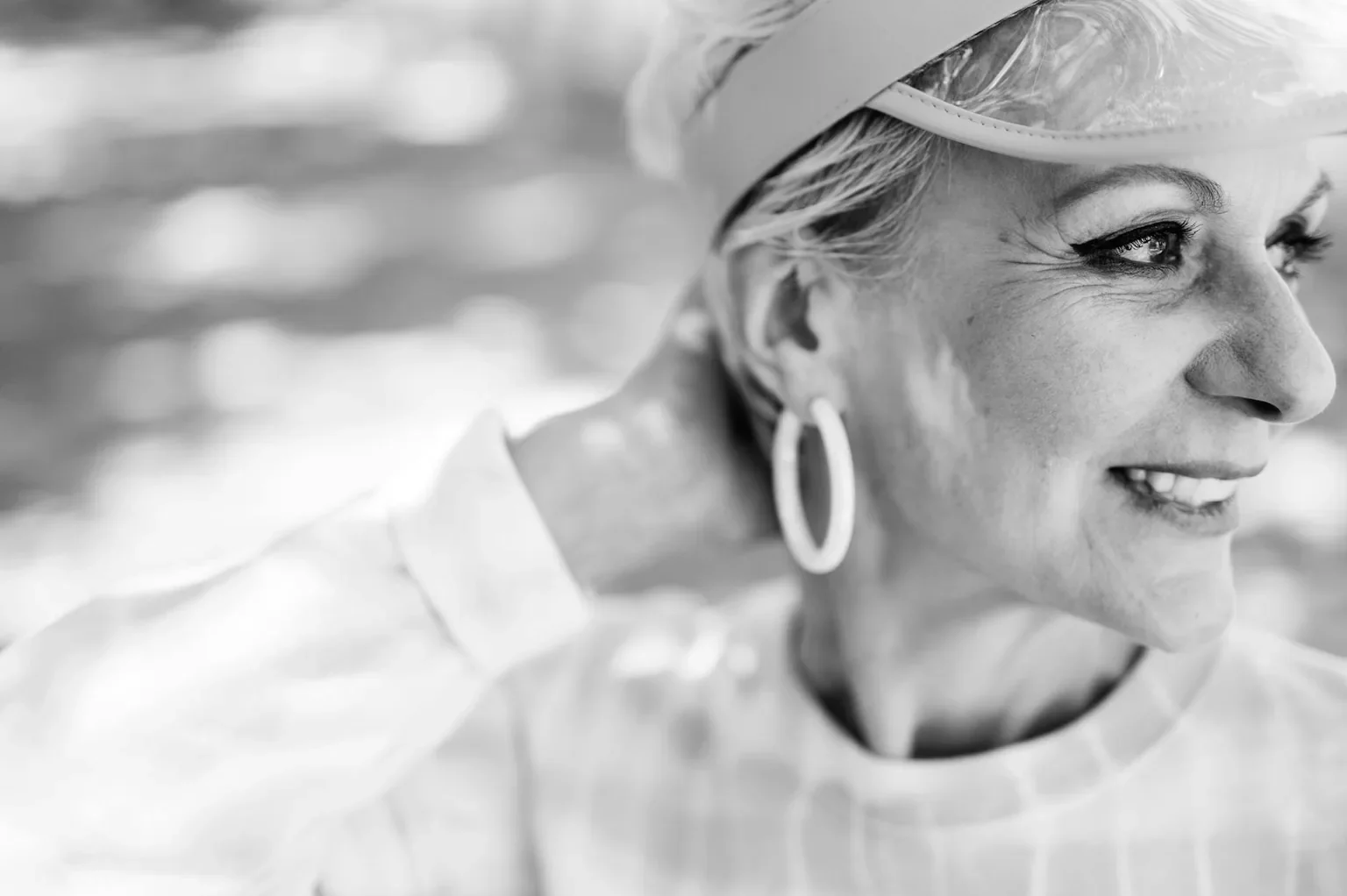 A smiling senior woman with an earring, captured in a classic black and white close-up portrait.