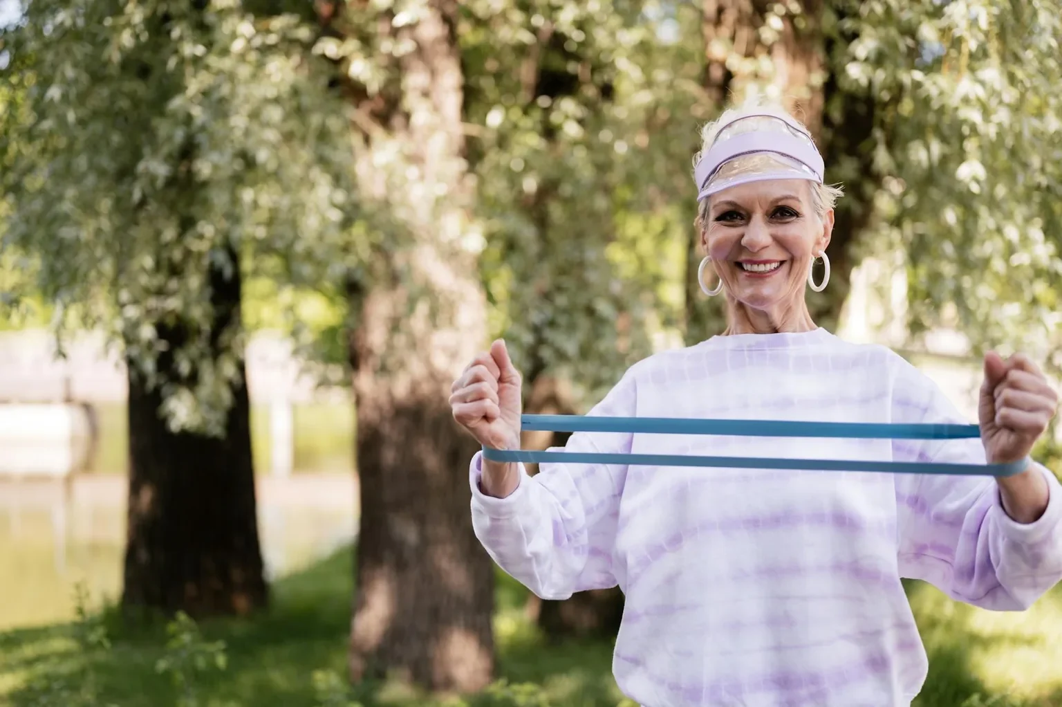 A cheerful senior woman engaging in fitness with a resistance band outdoors in a park setting.