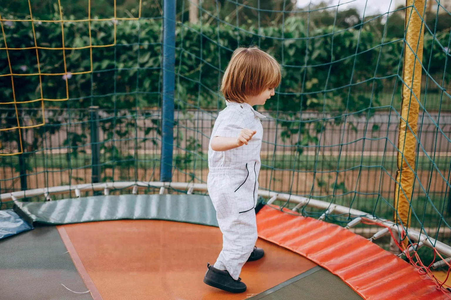 Young child in overalls playing on a colorful trampoline outside.