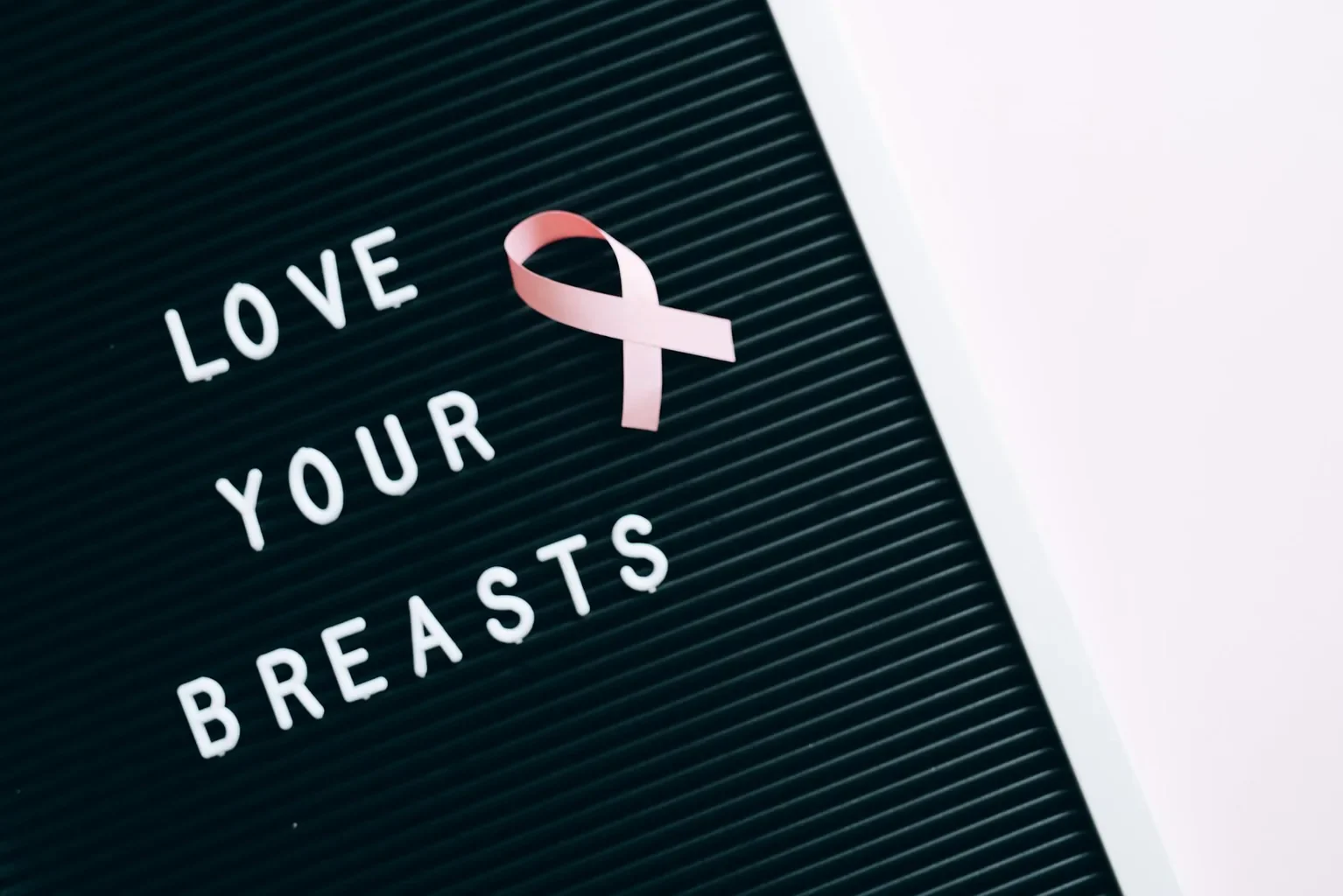 Pink ribbon and inspirational message "Love Your Breasts" on letter board for breast cancer awareness.