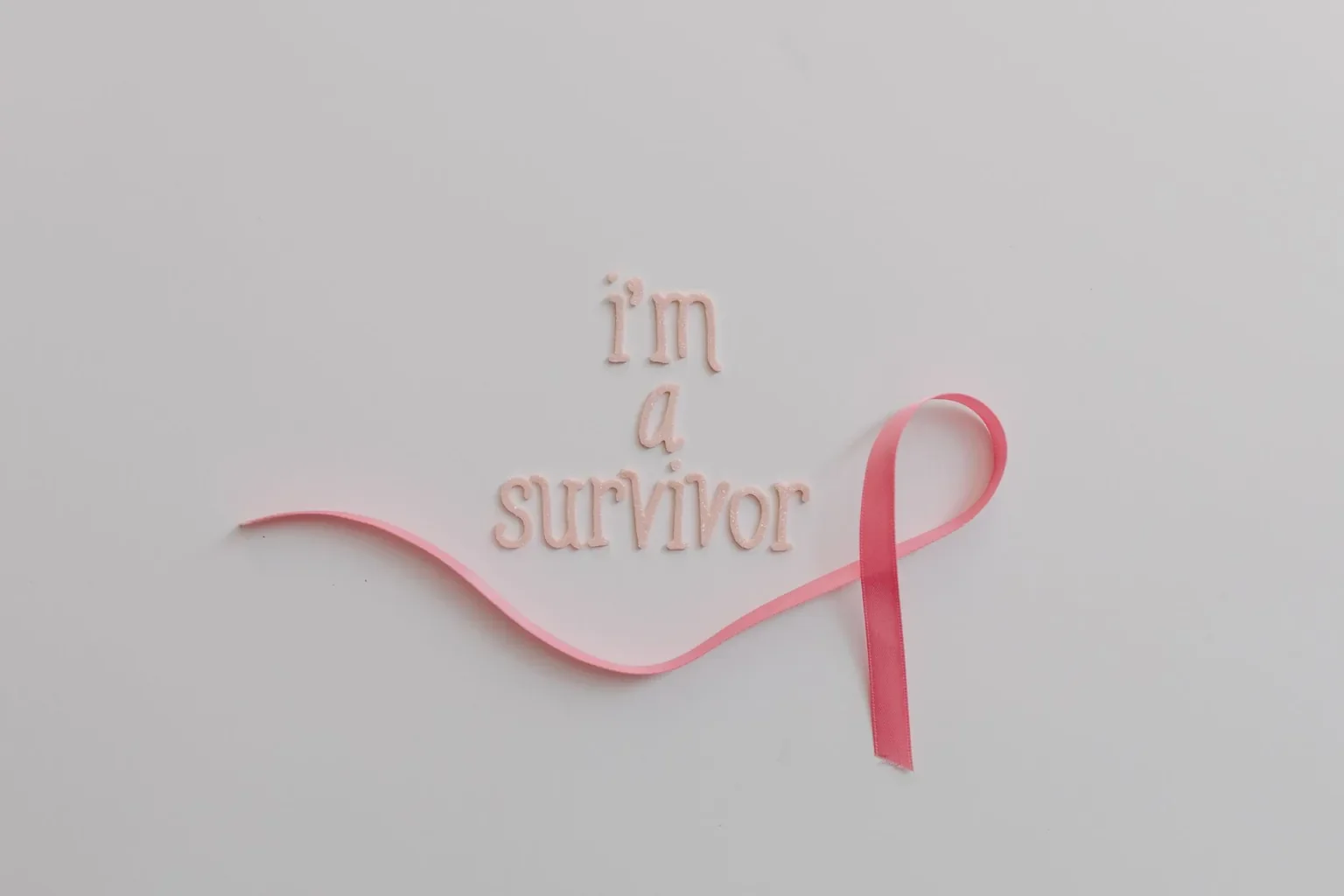 Pink ribbon with 'I'm a survivor' message symbolizing breast cancer awareness on white background.