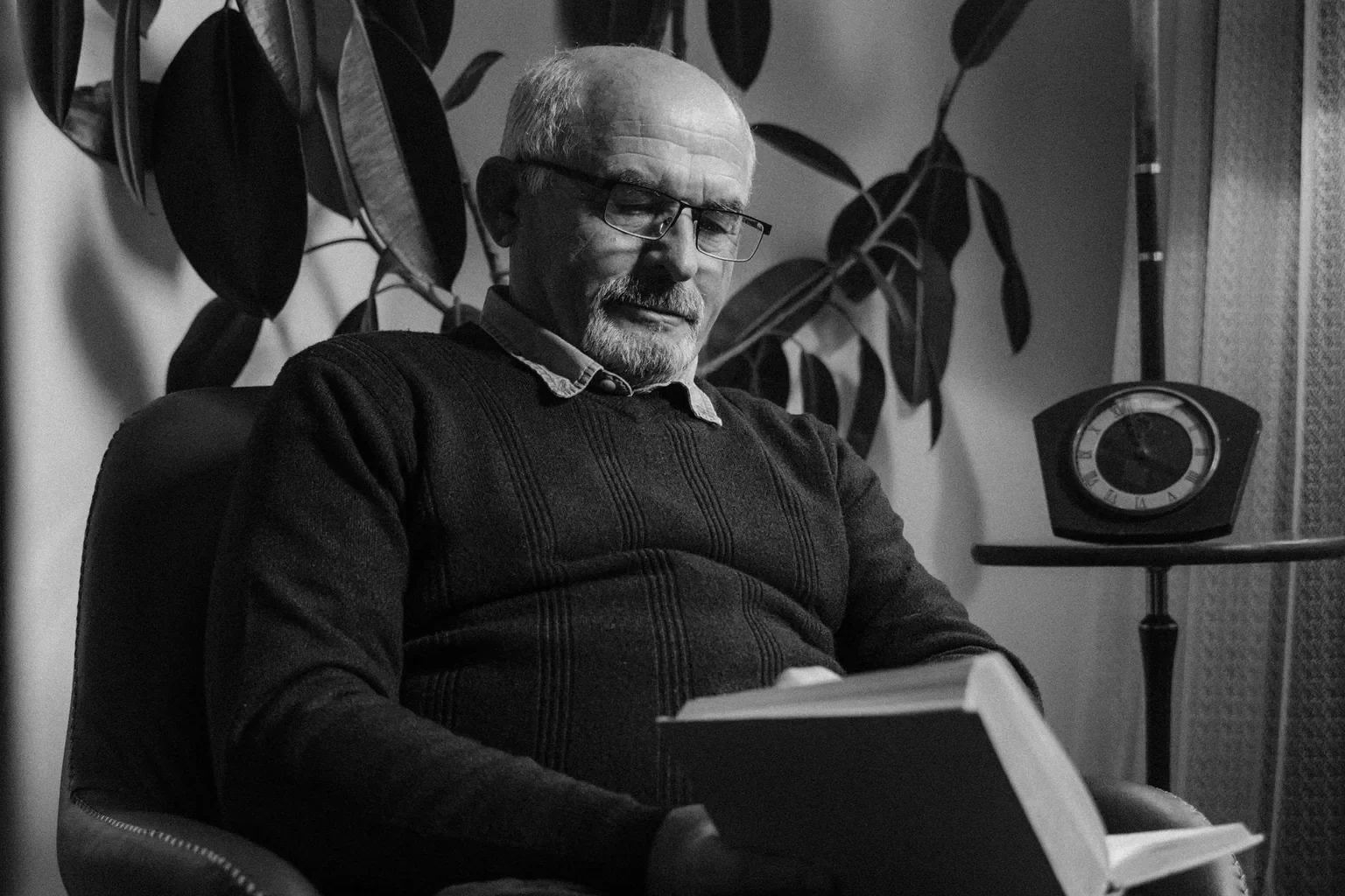 Monochrome portrait of an elderly man reading in an indoor setting, showcasing leisure and relaxation.